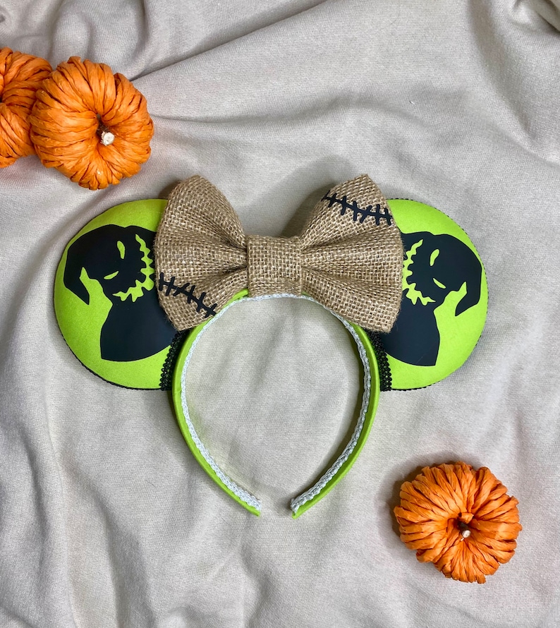 May include: Green and black mouse ears with a burlap bow. The ears feature a silhouette of Jack Skellington from The Nightmare Before Christmas.