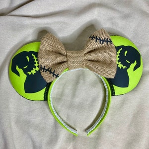 May include: Green and black mouse ears with a burlap bow. The ears feature a silhouette of Jack Skellington from The Nightmare Before Christmas.