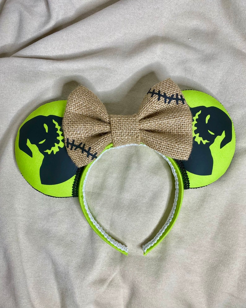 May include: Green and black mouse ears with a burlap bow. The ears feature a silhouette of Jack Skellington from The Nightmare Before Christmas.
