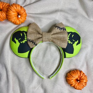 May include: Green and black mouse ears with a burlap bow. The ears feature a silhouette of Jack Skellington from The Nightmare Before Christmas.