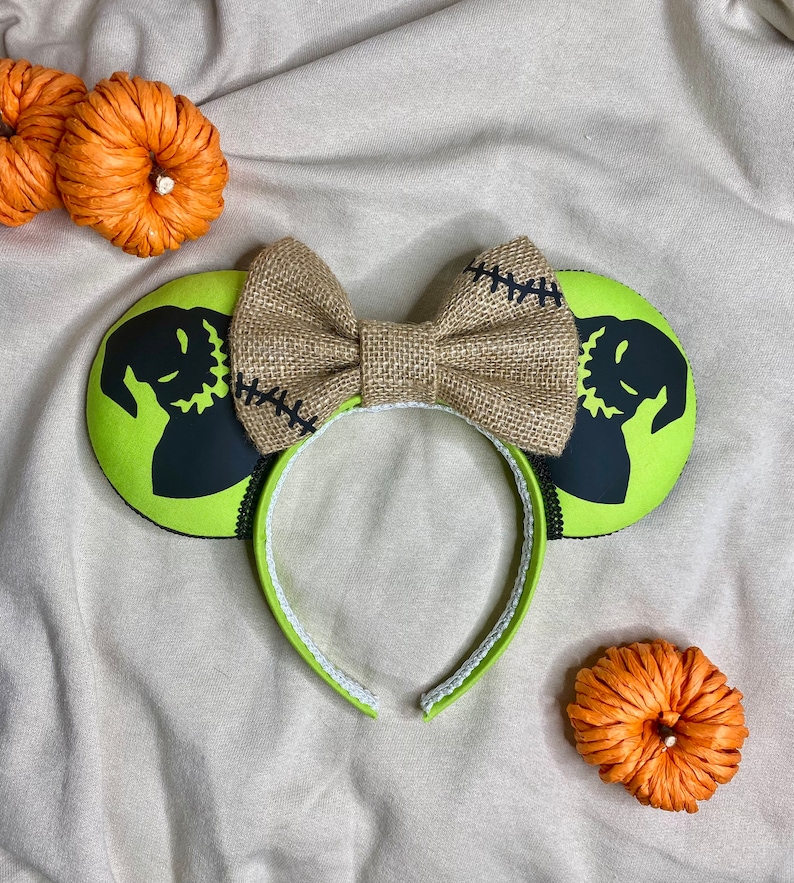 May include: Green and black mouse ears with a burlap bow. The ears feature a silhouette of Jack Skellington from The Nightmare Before Christmas.