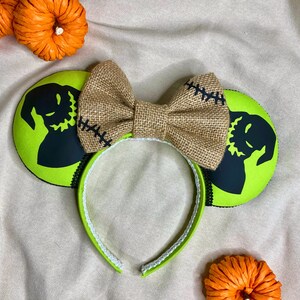 May include: Green and black mouse ears with a burlap bow. The ears feature a silhouette of Jack Skellington from The Nightmare Before Christmas.