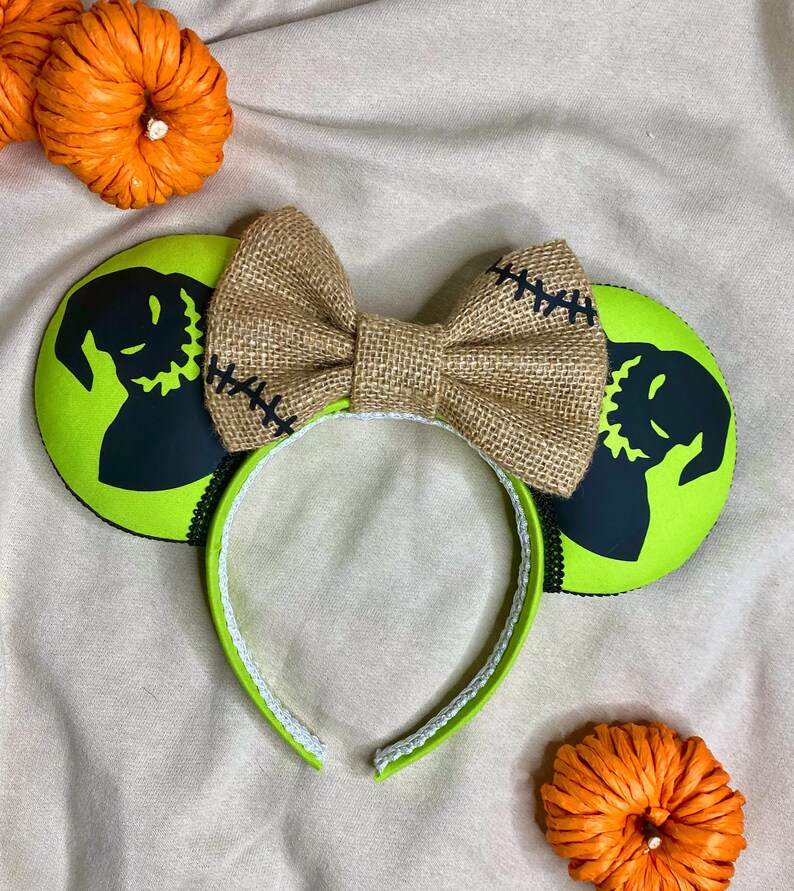May include: Green and black mouse ears with a burlap bow. The ears feature a silhouette of Jack Skellington from The Nightmare Before Christmas.