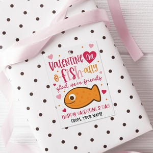 Digital download valentine tag featuring a charming pink fish, bold script fonts, and tiny hearts on a white background, including “Happy Valentine’s Day” and “From: Your Name,” used as a printable label to decorate school party favor bags or classroom exchange treats.