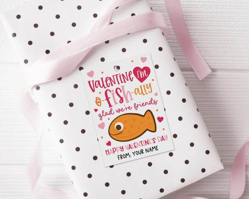 Digital download valentine tag featuring a charming pink fish, bold script fonts, and tiny hearts on a white background, including “Happy Valentine’s Day” and “From: Your Name,” used as a printable label to decorate school party favor bags or classroom exchange treats.