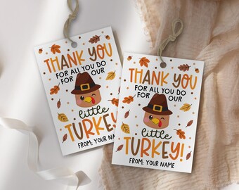 Könnte beinhalten: Zwei weiße Geschenkanhänger mit Thanksgiving-Motiv. Jeder Anhänger zeigt den Text "THANK YOU" und "little TURKEY!" in Orange und Braun, mit einem Cartoon-Truthahn mit Pilgerhut. Herbstblätter sind um das Design verstreut.