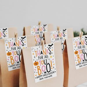 Pink and orange Halloween tag with large playful typography, white ghosts, a smiling orange pumpkin, black bat, spider, stars, and candy corn accents.