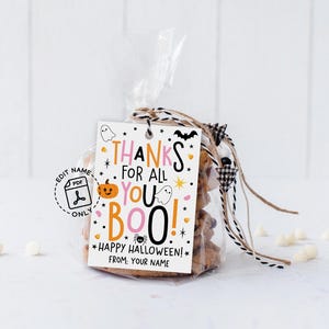 Vertical white gift tag hanging from twine on beige gift wrap, with colorful pink and orange lettering and cheerful Halloween graphics around the message.