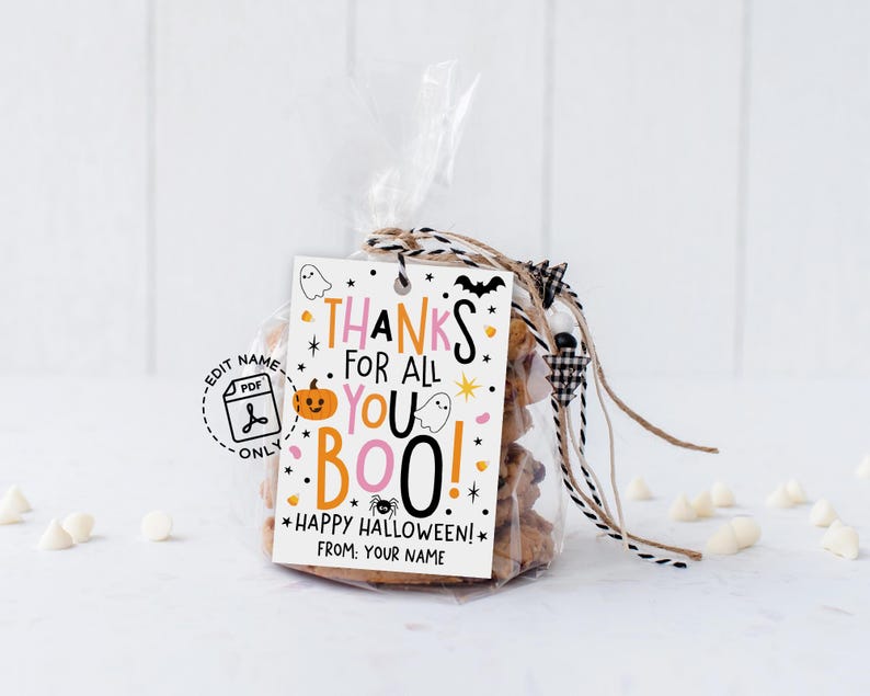 Vertical white gift tag hanging from twine on beige gift wrap, with colorful pink and orange lettering and cheerful Halloween graphics around the message.