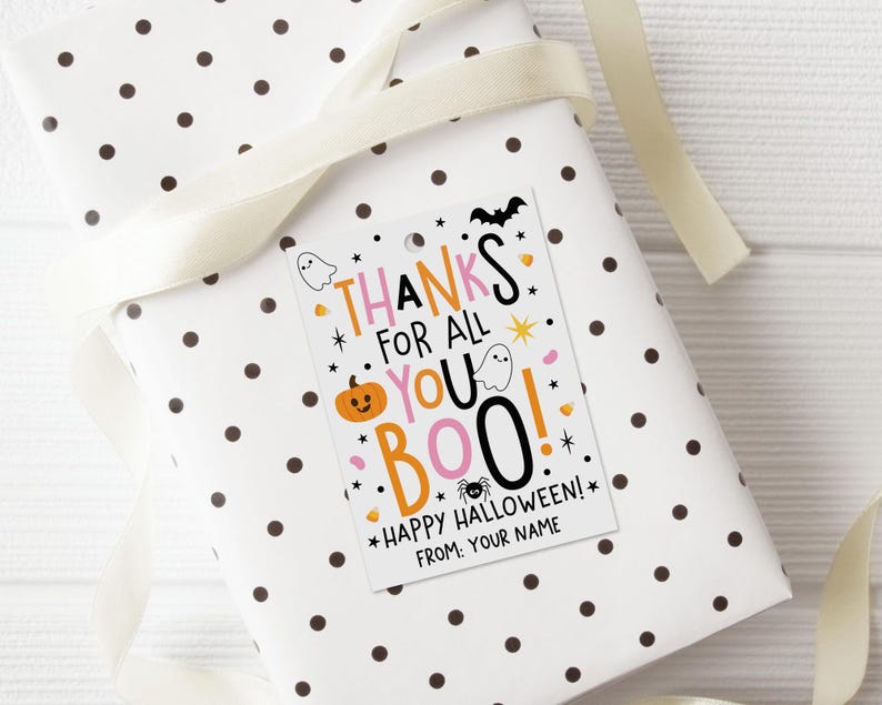 Pink, orange, and black Halloween gift tag displayed on a wrapped present, with candy corn, ghosts, a smiling pumpkin, bat, spider, and scattered stars.