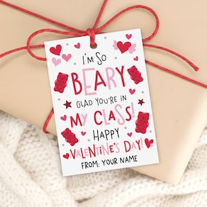 May include: A Valentine's Day gift tag with the text "I'm So Beary Glad You're in My Class! Happy Valentine's Day!" and space for a name. The tag features red gummy bear illustrations, hearts, and stars, tied with red twine.