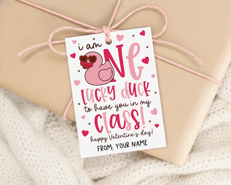 Cute classroom Valentine gift tag printable featuring the phrase “i am ONE LUCKY DUCK to have you in my CLASS!” with a cartoon duck, pink and red hearts, and playful mixed fonts, designed to be printed, trimmed, and clipped to student treat bags or school party goodies.