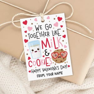 May include: A Valentine's Day gift tag with the text "WE GO TOGETHER LIKE MILK & COOKIES" in red and pink. The tag features illustrations of a glass of milk and a cookie wearing heart-shaped glasses. The tag is tied with twine.