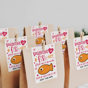 Kids classroom valentine printable tag that reads “You are o-fish-ally awesome” with “Happy Valentine’s Day” and “From: Your Name,” decorated with a smiling pink fish and scattered hearts, designed to be printed, cut, and attached to brown paper gift bags or snack favors.