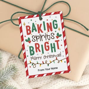 May include: A rectangular Christmas gift tag with the words "BAKING spirits BRIGHT Merry Christmas!" in red and green. The tag has a red and white striped border and is tied to a wrapped gift with green twine.