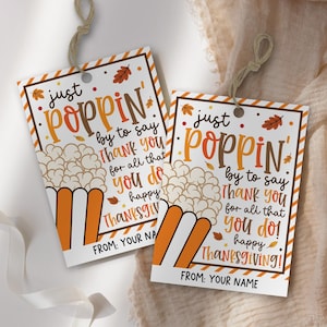 以下が含まれることがあります： ポップコーンのデザインと「just POPPIN' by to say THANK YOU for all that you do! happy THANKSGIVING!」というテキストがオレンジ、茶色、黄色の長方形のギフトタグが2つ。 タグには吊り下げ用の紐が付いています。