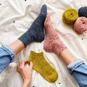 May include: Three pairs of hand-knitted socks in different colors: blue, pink, and yellow. The socks are shown on a white background.