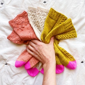 Könnte beinhalten: Vier Paar gestrickte Socken in verschiedenen Farben, darunter rosa, pfirsich, creme und gelb. Die Socken haben ein Spitzenmuster und einen rosa Saum oben.