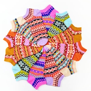 Op de afbeelding: Een verzameling kleurrijke gebreide sokken, gerangschikt in een cirkelvormig patroon. De sokken hebben verschillende geometrische en bloemmotieven in roze, blauw, oranje, groen en paars. De sokken zijn gemaakt van een zacht, warm materiaal.