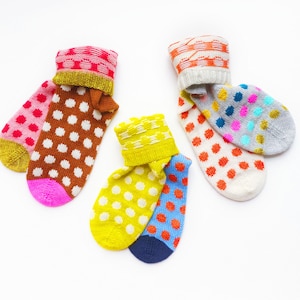 Peut inclure: Trois paires de chaussettes en tricot colorées avec des motifs de pois. Les chaussettes sont dans des tons de rose, marron, jaune, bleu, orange et gris.