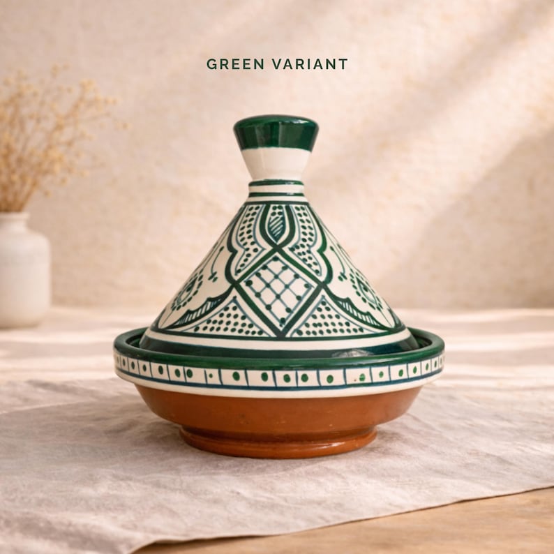 Op de afbeelding: Een groene en witte keramische tajinepot met een conische deksel en een ronde basis. De deksel heeft ingewikkelde groene patronen en de basis is warmbruin van kleur. De tekst "GREEN VARIANT" staat bovenaan.