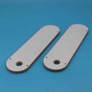 May include: Two white wooden router templates with the text "ZERO INSERT" printed on them. The templates have a large hole in the centre and several smaller holes around the edges.