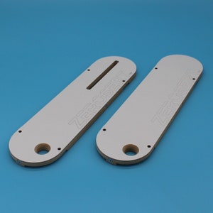 May include: Two white wooden router templates with the text "ZERUSERT" printed on them. The templates are designed for use with a router to create precise cuts in wood.