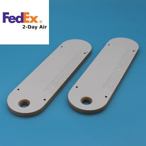 May include: Two white, rectangular, wooden templates with the text "ZERO USERT" printed on them. The templates are used for woodworking projects.