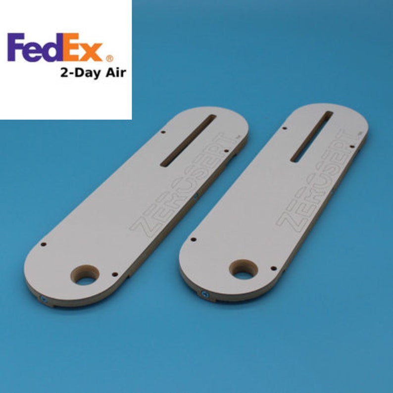 May include: Two white, rectangular, wooden router templates with the text "ZeroInsert" printed on them. The templates have a slot in the center and a hole on each end.