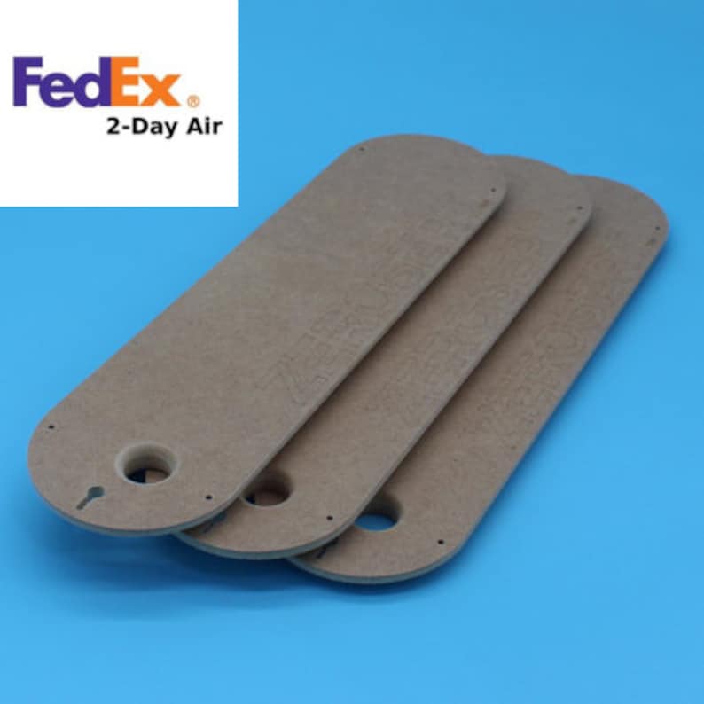 May include: Three elongated, light brown wooden pieces with rounded ends and a keyhole-shaped cutout. Each piece has small holes and text. The background is a solid blue. The FedEx logo and "2-Day Air" text are in the upper left corner.