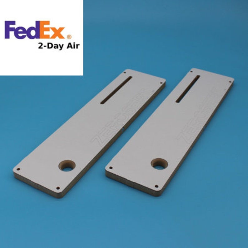 May include: Two white wooden router jigs with a slot and a hole in the center. The jigs are labeled "ZERO SR", and are used for woodworking projects.