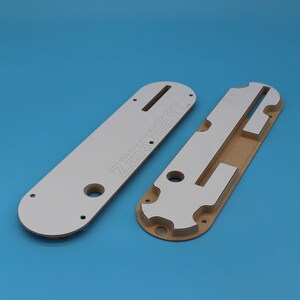 Puede incluir: Dos plantillas de fresado de madera blanca y marr&oacute;n con el texto "ZERO-SERT" impreso en una de las plantillas.