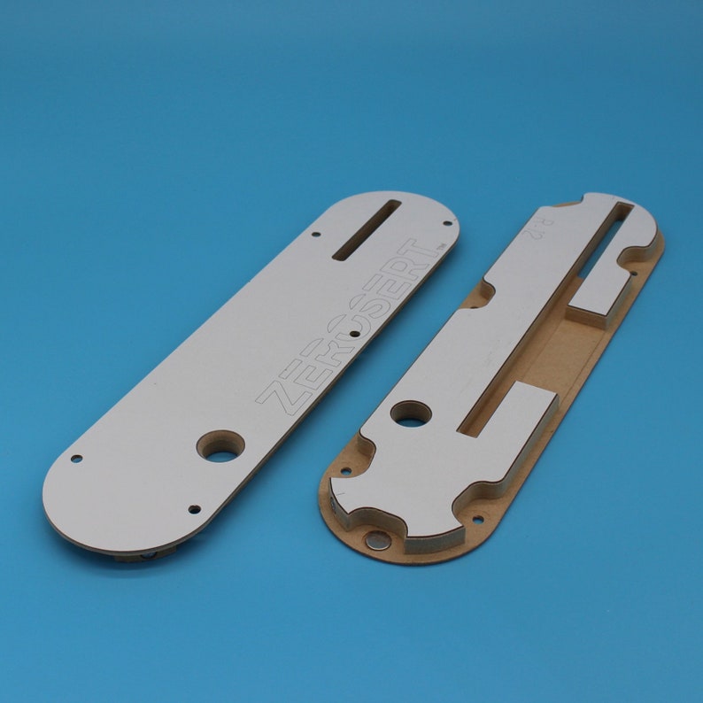 Puede incluir: Dos plantillas de fresado de madera blanca y marr&oacute;n con el texto "ZERO-SERT" impreso en una de las plantillas.