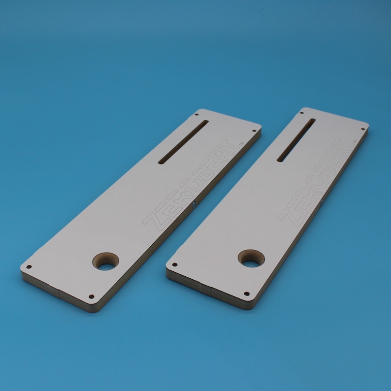 May include: Two white wooden router templates with the text "ZERO SR" printed on them. Each template has a slot and a hole.