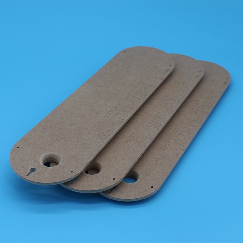 May include: Three light brown, elongated wooden pieces with rounded ends and a keyhole-shaped opening. The word "ZERKUSE" is etched into each piece. The items are arranged on a blue background.