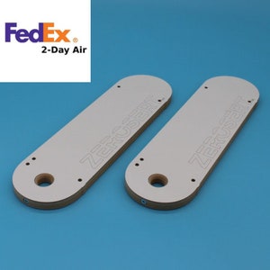May include: Two white wooden router templates with the text "ZERO INSERT" printed on them. The templates have a hole in the center and several smaller holes around the edges.