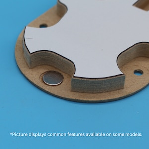 May include: Close-up of a light brown, multi-layered object with a white top layer and a silver disc. The object has a unique shape with rounded edges and cut-out sections. The text at the bottom says "Picture displays common features available on some models."