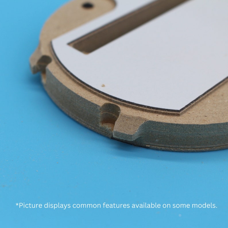 Puede incluir: Primer plano de una base redonda de madera con un inserto rectangular blanco. La base tiene una superficie texturizada y un peque&ntilde;o agujero en el centro. El inserto tiene una ranura cortada.