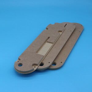 May include: Three wooden table saw inserts, each with a unique shape and cutouts. The inserts are a light brown color and are stacked on top of each other against a blue background. Each insert has a different design.