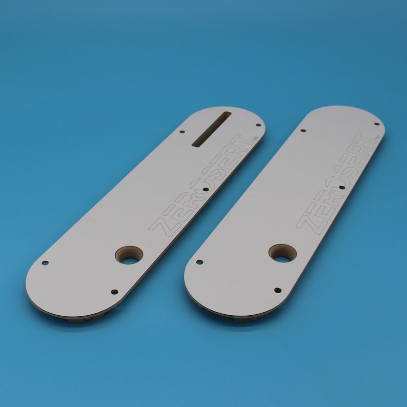 Może przedstawiać: Dwa białe, prostokątne szablony frezarskie z nadrukiem "ZERO INSERT". Szablony mają otw&oacute;r w środku i szczelinę z jednej strony.