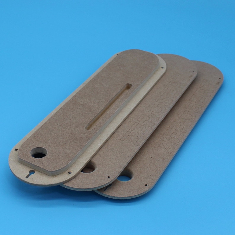 May include: Three beige wooden table saw inserts with a keyhole and a slot cut out. The inserts are stacked on a blue background. The text "ZERO CLEARANCE" is visible on the top insert.