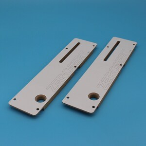 May include: Two white wooden jigs with the text "ZERUSERT" printed on them. The jigs have a slot and a hole in the centre.