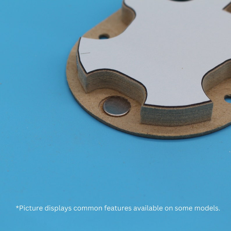 May include: Close-up of a white, round, multi-layered component with a black outline and a small, silver magnet attached to the bottom.