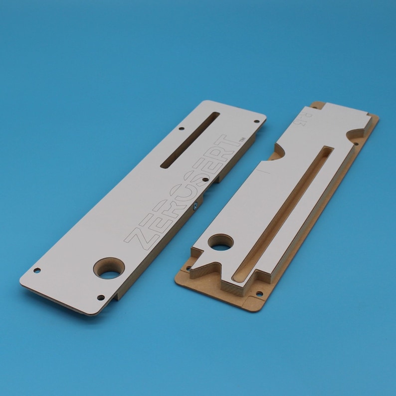 May include: Two white wooden templates for woodworking projects. The larger template has the word "ZERCSERT" printed on it. The smaller template has a cutout for a drawer slide.