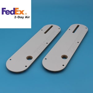 May include: Two white plastic templates for woodworking, each with the text "Zero-Clear" printed on them. The templates are designed for use with a router to create precise cuts.