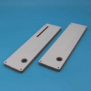 May include: Two white wooden router jigs with the text "ZERO INSERT" printed on them. The jigs have a hole and a slot cut out of them.