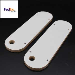 May include: Two white, rectangular, wooden templates with rounded edges and holes for a router bit. The templates have multiple holes for mounting.