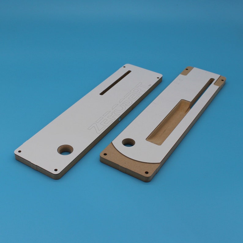 May include: Two white and brown wooden router jigs with cutouts and holes. The larger jig has the text "ZeroInsert" printed on it.