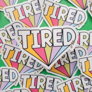 May include: A close-up of colorful stickers with the word "TIRED" printed in a rainbow font. The stickers are arranged in a random pattern on a green background.