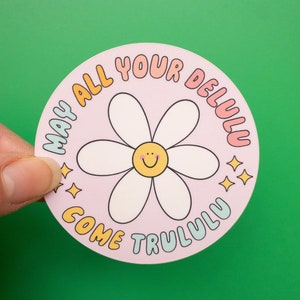 Könnte beinhalten: Ein runder Aufkleber in Rosa und Weiß mit einer Gänseblümchen und dem Text "May all your delulu come trululu".